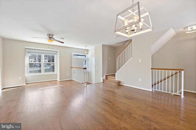 unfurnished living room featuring baseboards, stairs, ceiling fan, and wood finished floors