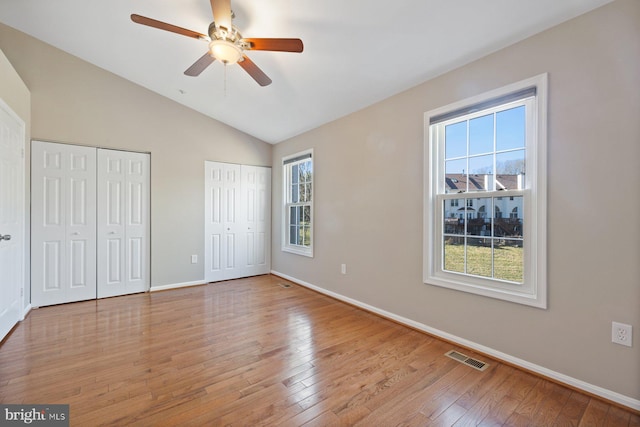 unfurnished bedroom featuring baseboards, visible vents, lofted ceiling, wood-type flooring, and two closets