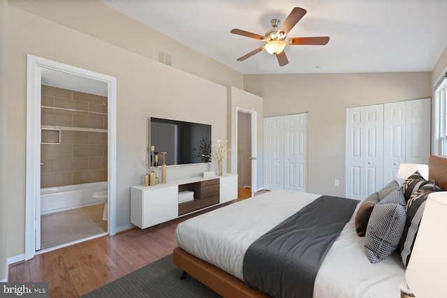 bedroom featuring wood finished floors, visible vents, vaulted ceiling, ensuite bathroom, and two closets