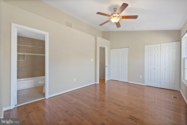 unfurnished bedroom with visible vents, two closets, baseboards, vaulted ceiling, and wood finished floors