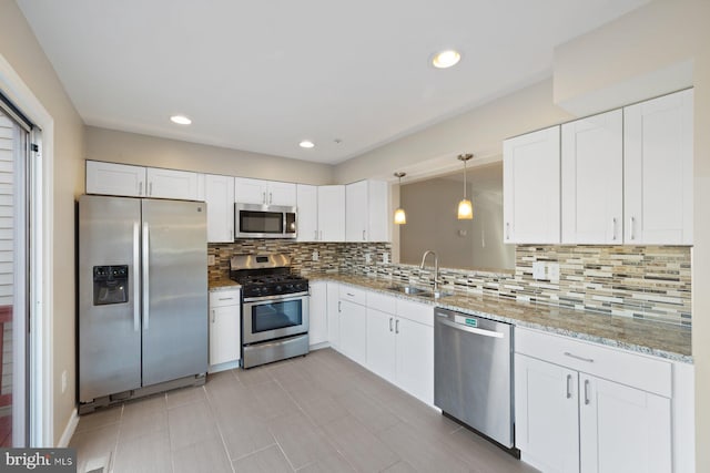 kitchen featuring light stone counters, decorative backsplash, appliances with stainless steel finishes, white cabinets, and a sink