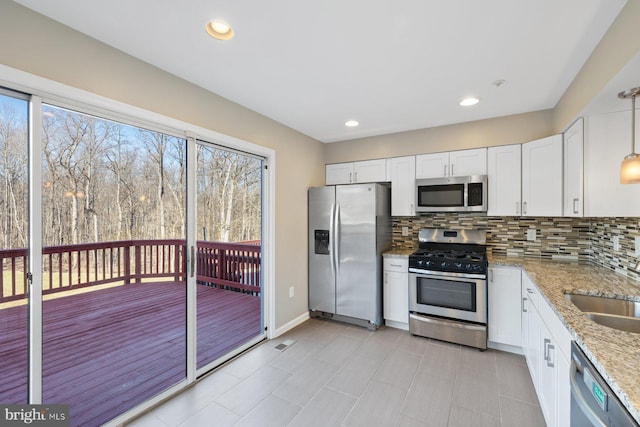 kitchen featuring light stone countertops, backsplash, appliances with stainless steel finishes, and white cabinetry