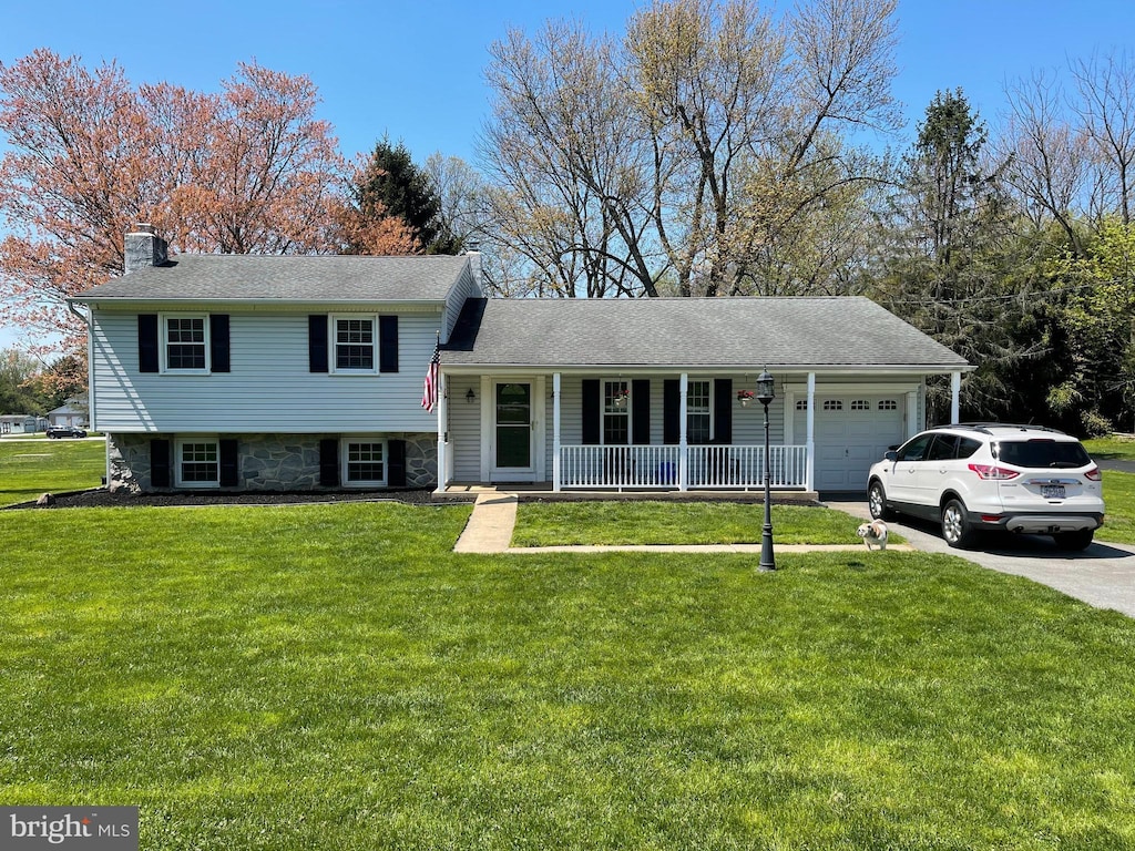 tri-level home featuring concrete driveway, a front yard, covered porch, a chimney, and a garage