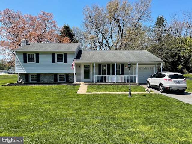 tri-level home featuring concrete driveway, a front yard, covered porch, a chimney, and a garage