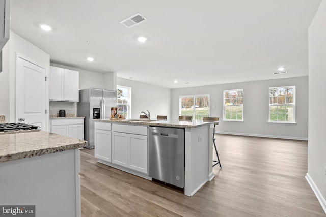 kitchen featuring visible vents, an island with sink, a sink, white cabinets, and appliances with stainless steel finishes