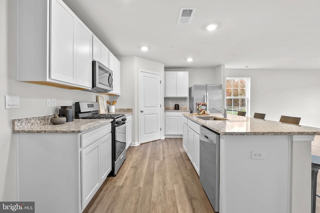 kitchen featuring visible vents, a kitchen island with sink, light wood-style flooring, a sink, and stainless steel appliances