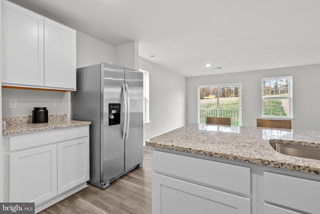 kitchen featuring stainless steel refrigerator with ice dispenser, a sink, white cabinetry, light wood-style floors, and light stone countertops