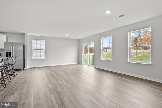 unfurnished living room featuring light wood-style flooring, baseboards, and a wealth of natural light