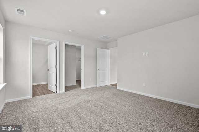 unfurnished bedroom featuring a walk in closet, carpet, visible vents, and baseboards