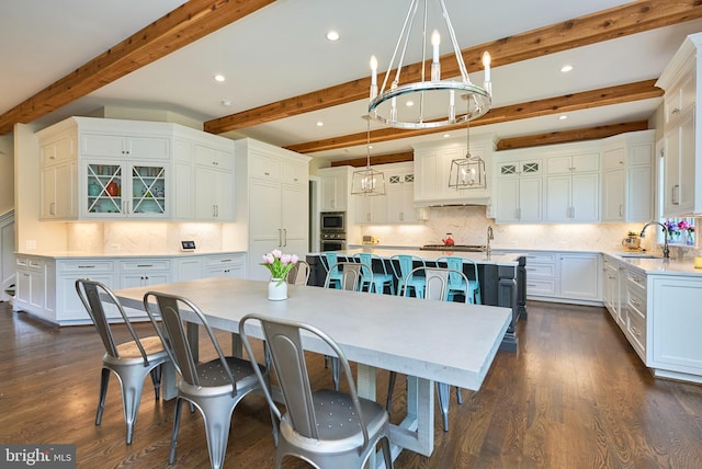 kitchen featuring a breakfast bar, pendant lighting, a sink, a large island with sink, and dark wood-style flooring