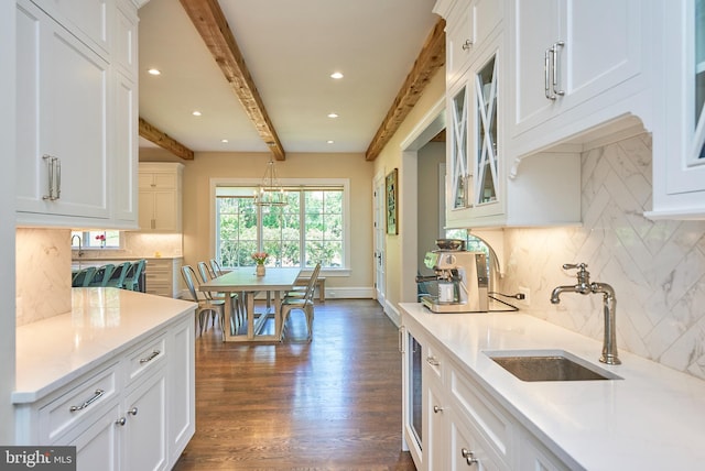 kitchen featuring beam ceiling, white cabinets, and a sink