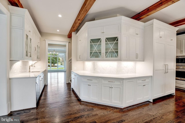 kitchen with beam ceiling, white cabinetry, light countertops, and stainless steel oven