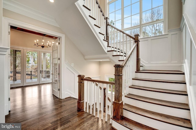 stairs with a wainscoted wall, a notable chandelier, ornamental molding, wood finished floors, and a decorative wall