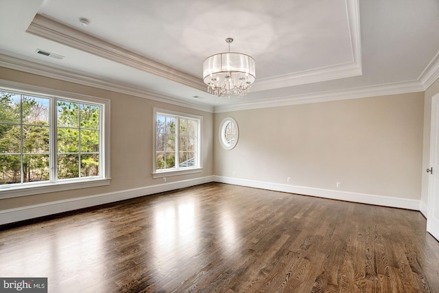 spare room with visible vents, an inviting chandelier, a tray ceiling, and wood finished floors