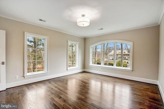 spare room with baseboards, wood finished floors, visible vents, and ornamental molding