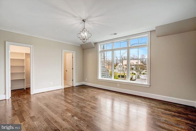 unfurnished bedroom with ornamental molding, wood finished floors, an inviting chandelier, baseboards, and a spacious closet