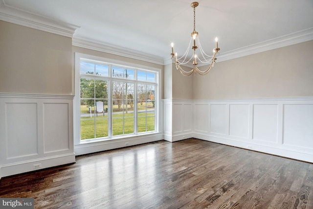 unfurnished dining area featuring dark wood-style floors, wainscoting, crown molding, and an inviting chandelier