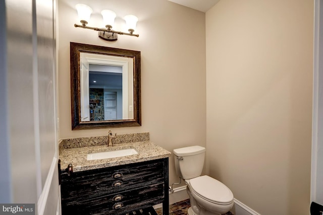 half bathroom with baseboards, toilet, and vanity