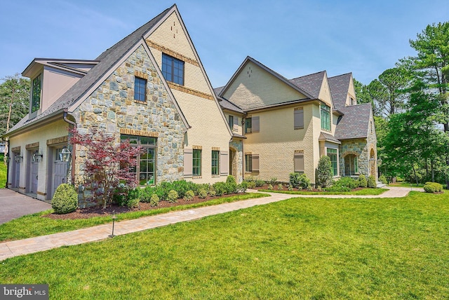 view of front of house featuring brick siding, a front lawn, a garage, stone siding, and driveway