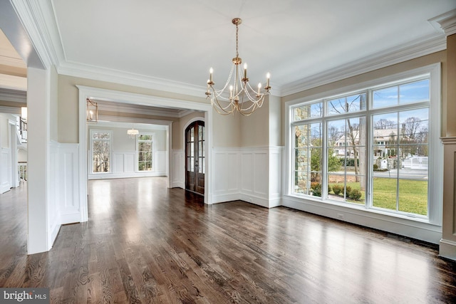 unfurnished dining area with a wealth of natural light, a notable chandelier, dark wood finished floors, and crown molding