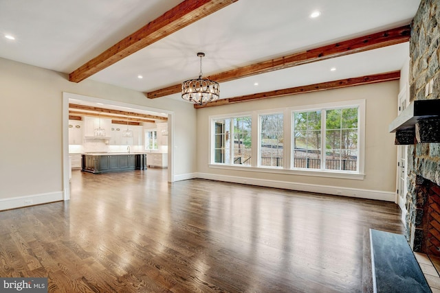 unfurnished living room featuring a notable chandelier, a stone fireplace, baseboards, and dark wood-style flooring