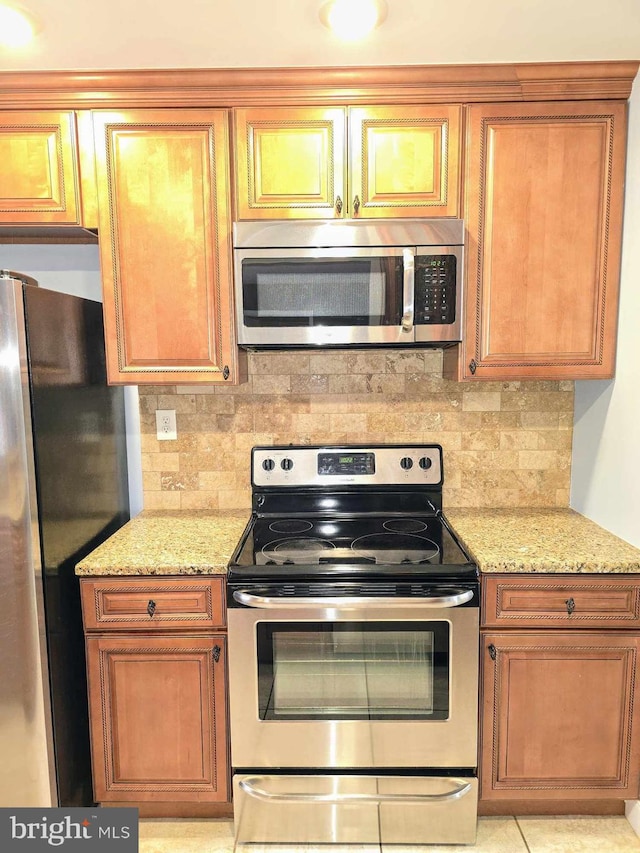 kitchen featuring light stone countertops, backsplash, appliances with stainless steel finishes, and brown cabinetry