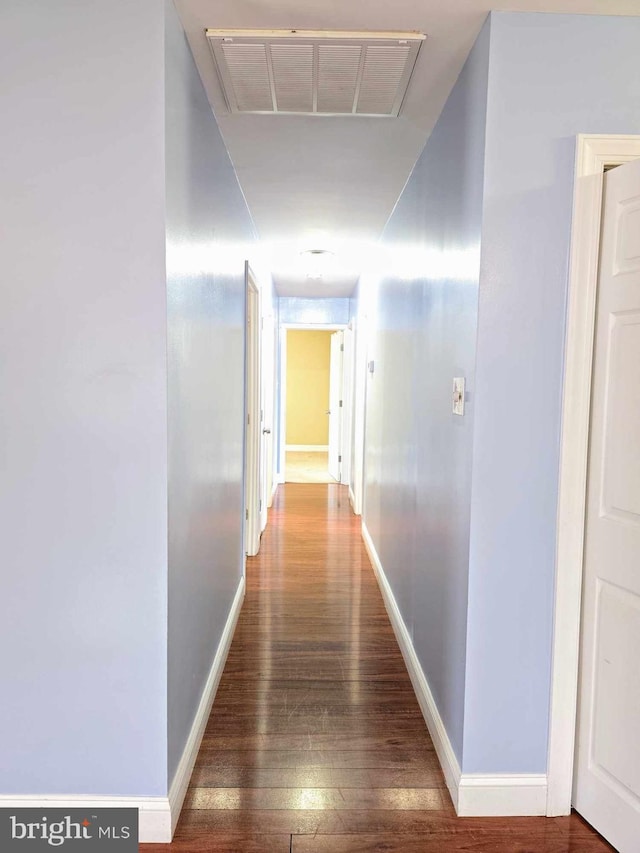 hallway featuring visible vents, baseboards, and hardwood / wood-style flooring