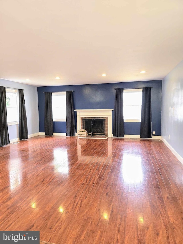 unfurnished living room featuring hardwood / wood-style floors, a brick fireplace, recessed lighting, and baseboards