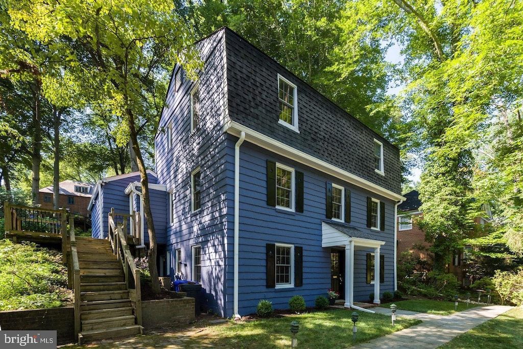 view of front of house featuring a front yard, stairway, and roof with shingles