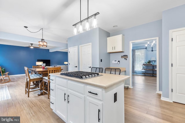 kitchen with light wood-style flooring, decorative light fixtures, a kitchen island, stainless steel gas stovetop, and a chandelier