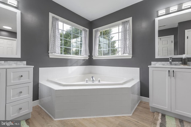 full bath featuring vanity, a garden tub, wood finished floors, and baseboards