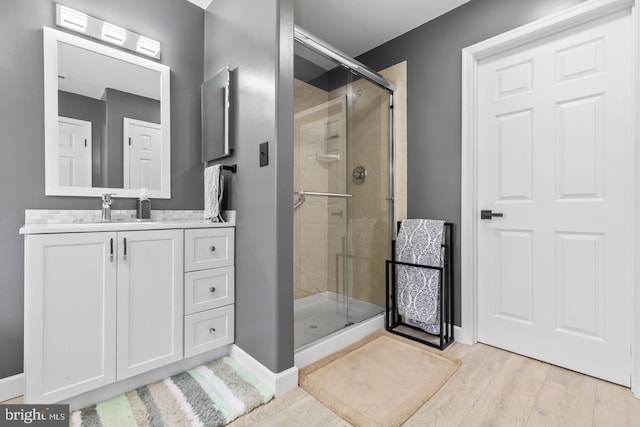 full bath with a shower stall, vanity, baseboards, and wood finished floors