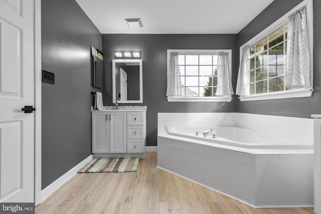 full bath featuring visible vents, a garden tub, wood finished floors, baseboards, and vanity