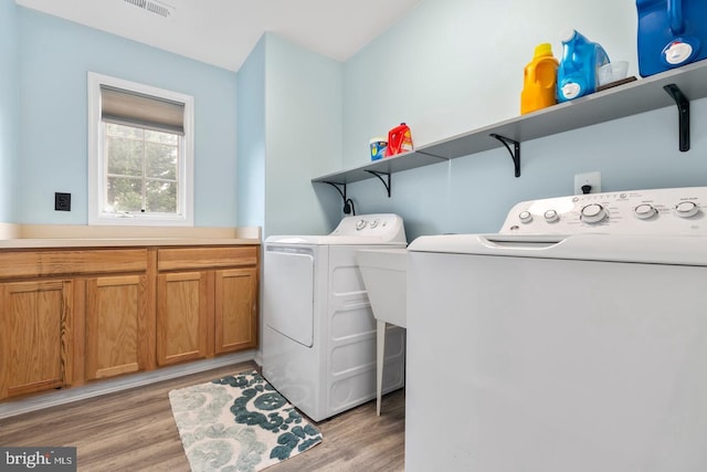 laundry room featuring washing machine and clothes dryer, visible vents, cabinet space, and light wood-type flooring