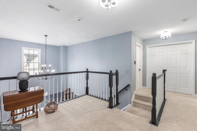 hallway with an upstairs landing, visible vents, carpet, and an inviting chandelier