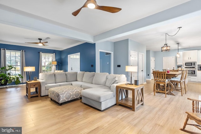 living area featuring beam ceiling, light wood-style flooring, baseboards, and ceiling fan