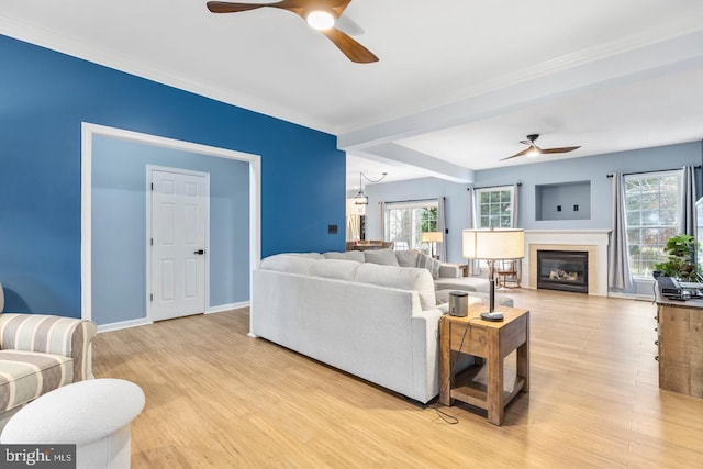 living area featuring a glass covered fireplace, baseboards, light wood-style floors, and ceiling fan