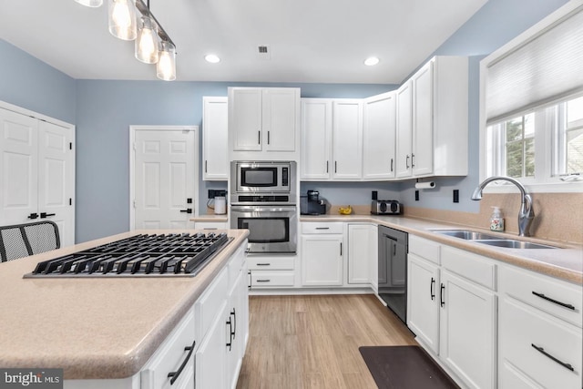 kitchen with light wood finished floors, light countertops, appliances with stainless steel finishes, white cabinets, and a sink