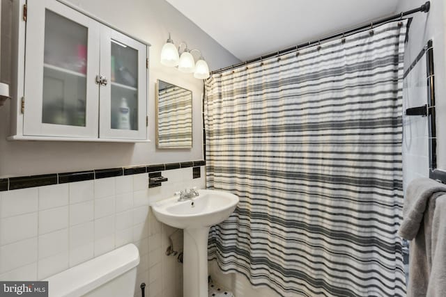 full bath with a wainscoted wall, toilet, a shower with shower curtain, tile walls, and a sink