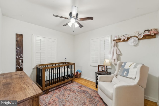 bedroom featuring baseboards, a nursery area, wood finished floors, and a ceiling fan