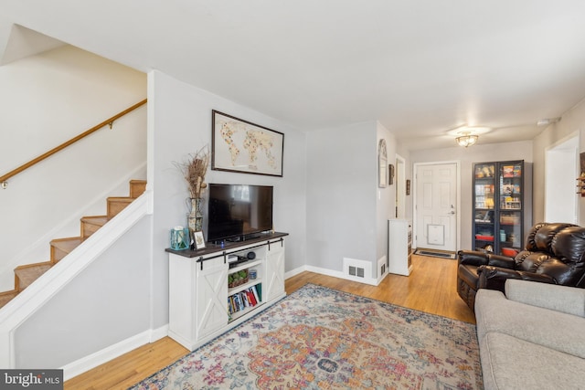 living room with visible vents, light wood-style flooring, stairs, and baseboards