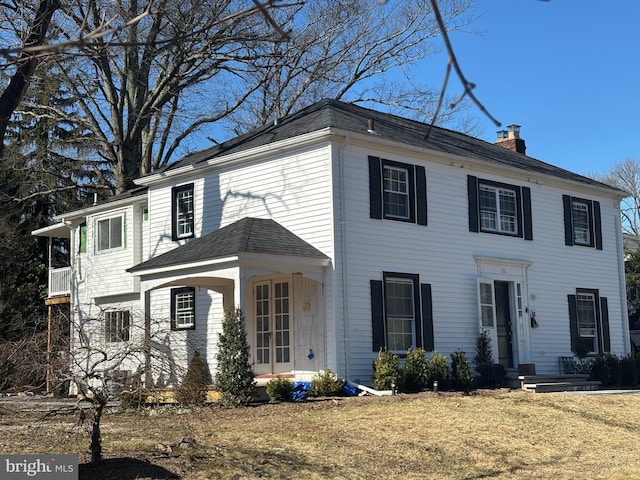 colonial home featuring roof with shingles and a chimney