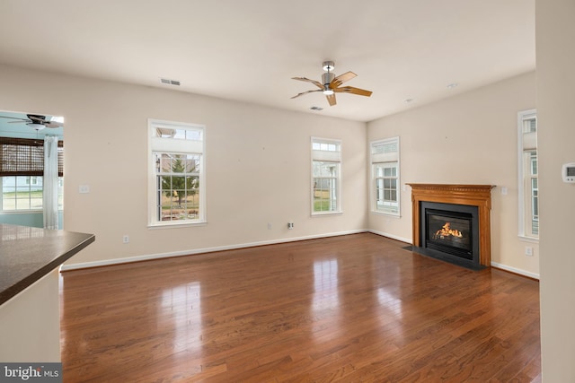 unfurnished living room with visible vents, baseboards, a fireplace with flush hearth, wood finished floors, and a ceiling fan