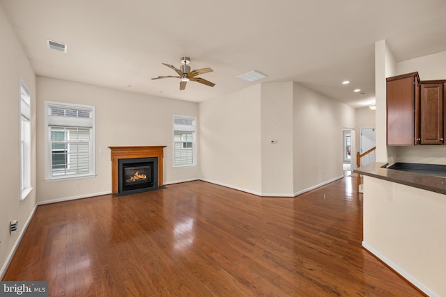 unfurnished living room featuring visible vents, baseboards, ceiling fan, a fireplace with flush hearth, and dark wood-style floors