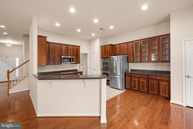 kitchen with a peninsula, dark countertops, light wood-type flooring, and appliances with stainless steel finishes