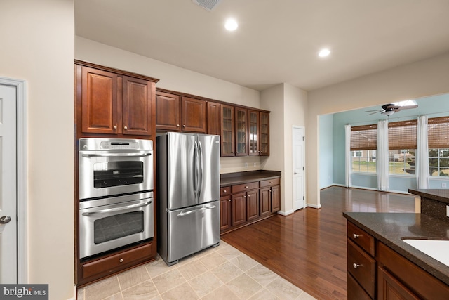 kitchen featuring glass insert cabinets, ceiling fan, recessed lighting, dark stone countertops, and stainless steel appliances