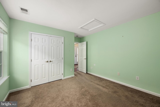 unfurnished bedroom with baseboards, visible vents, attic access, a closet, and carpet flooring