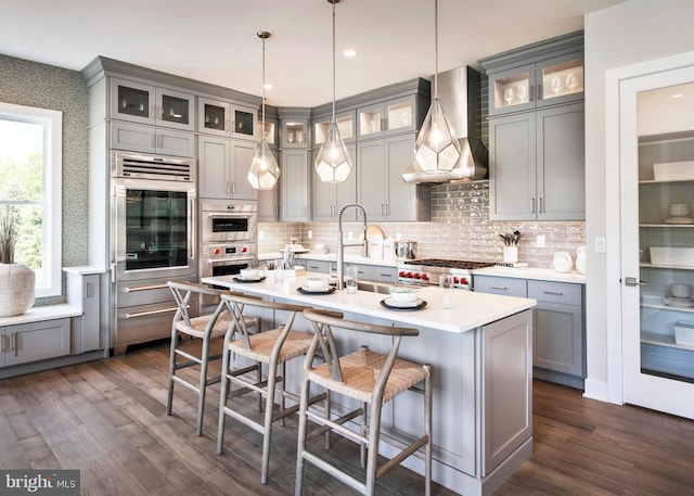 kitchen featuring dark wood finished floors, wall chimney exhaust hood, stainless steel double oven, and gray cabinetry