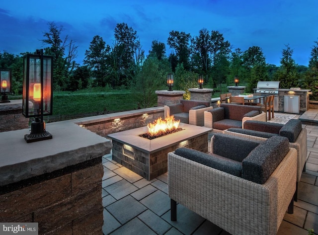 patio terrace at dusk featuring an outdoor living space with a fire pit and area for grilling