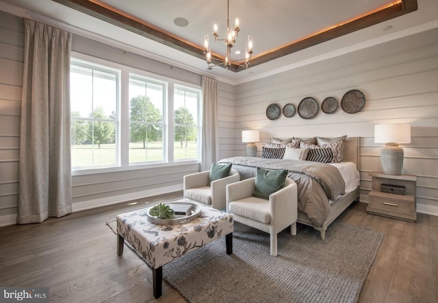 bedroom with a raised ceiling, a notable chandelier, and wood finished floors